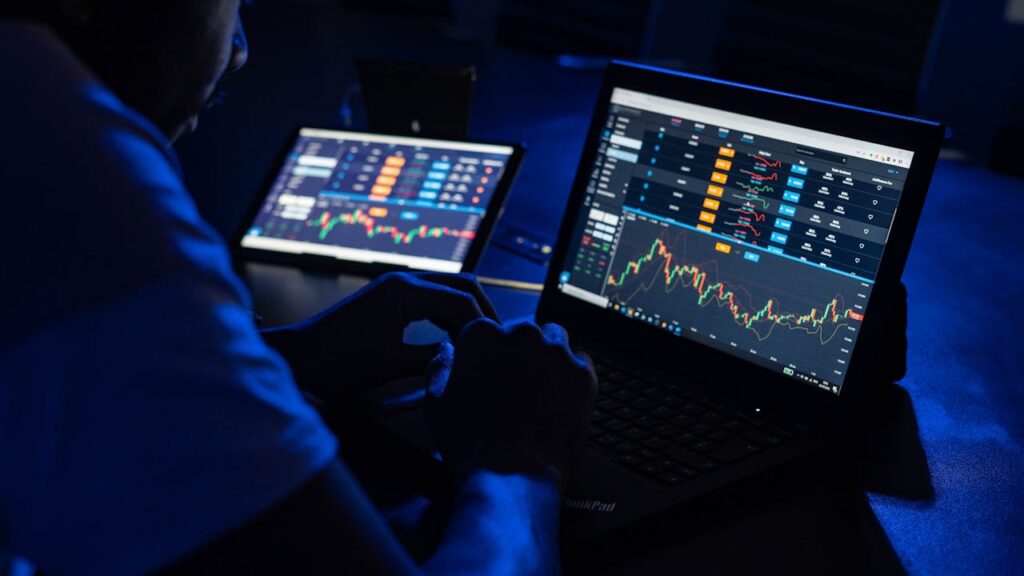 pexels-photo-18706593 Man analyzing financial charts and data on laptops in a dimly lit room, highlighting forex trading.